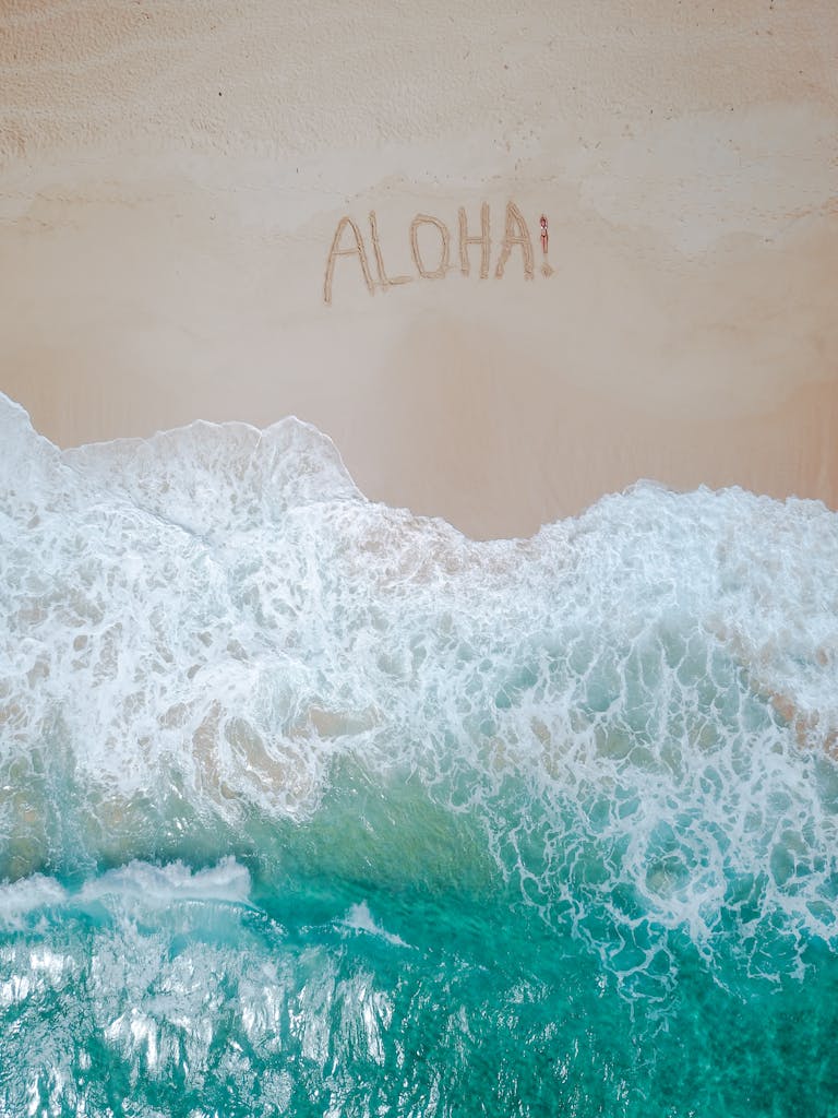A serene aerial shot of a tropical beach with 'Aloha' written in the sand and waves crashing ashore.